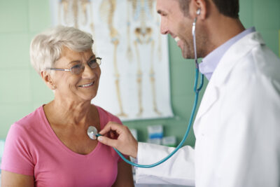 Male doctor listening to female patient's heart during routine physical exam